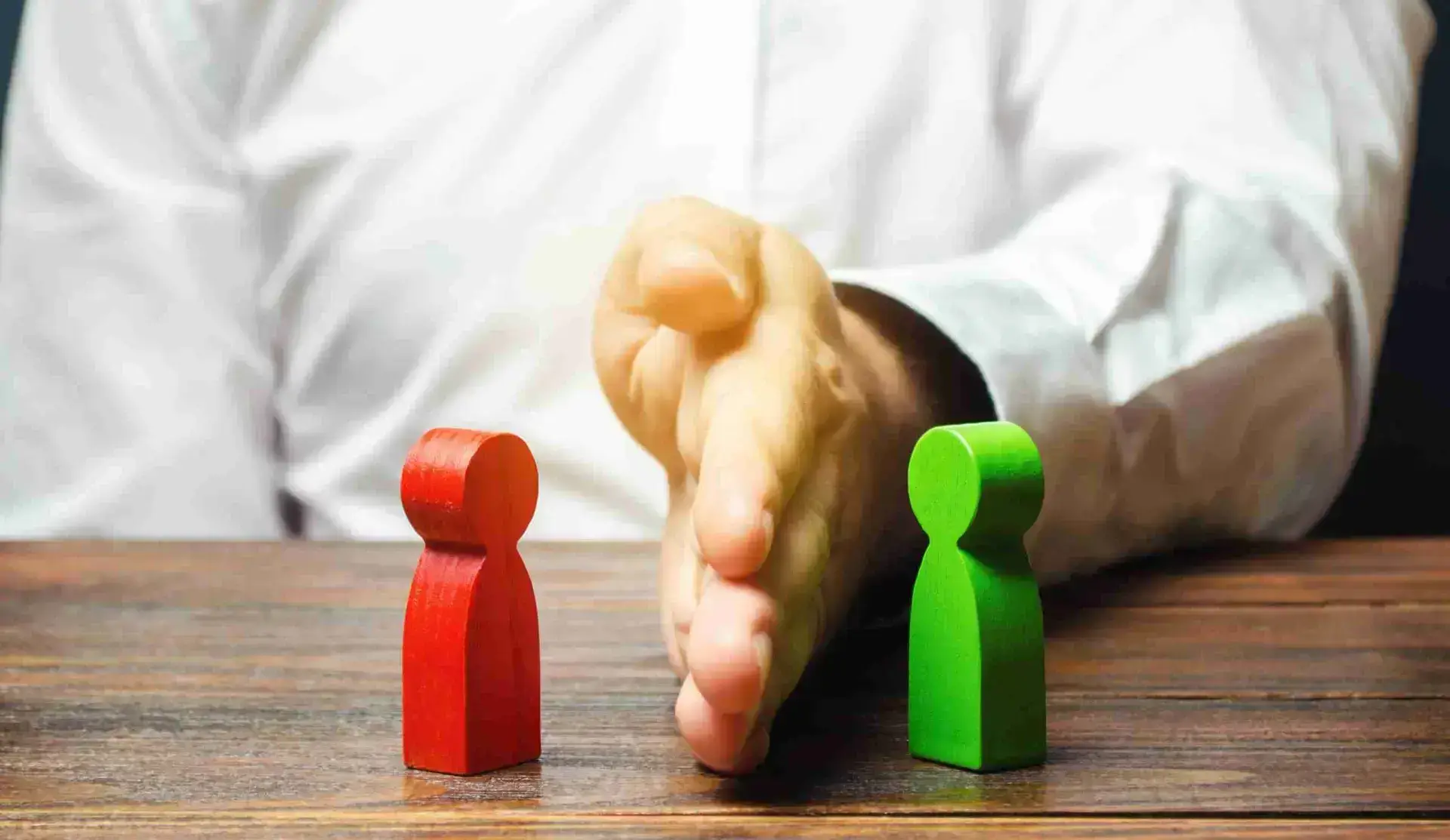 Two wooden figure colored red and green representing human and a hand separating them.