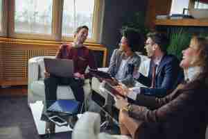 group of four people holding laptop and tablets laughing and talking together